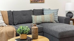 Un soggiorno moderno con un divano angolare grigio, un tavolino, una lampada, una pianta in vaso e un vaso decorativo.