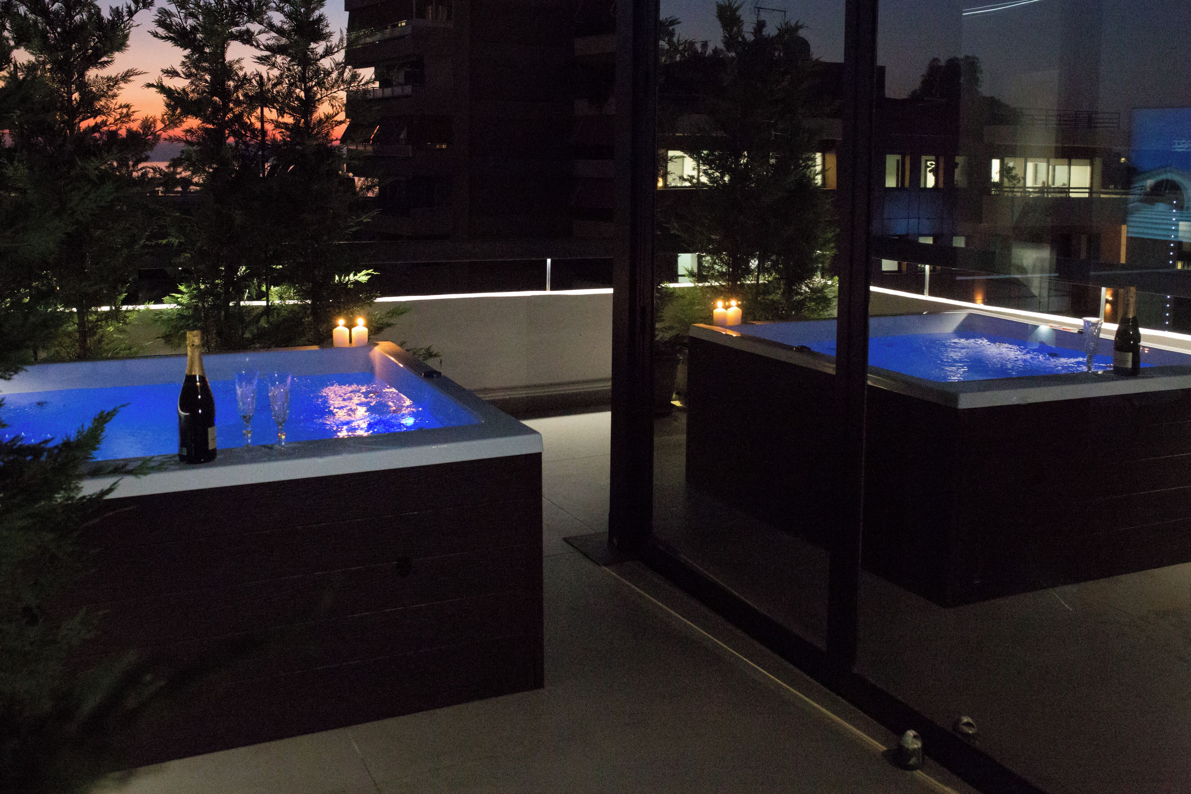 A rooftop hot tub with a bottle of champagne, candles, and a view of the cityscape at dusk.