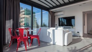 A modern living room with a white sofa, red chairs, a round table, and a large flat-screen TV. - Penthouse in the Heart of Glyfada (Glifada)