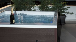A hot tub with a bottle of champagne and two glasses, surrounded by trees, with a sunset in the background. - Penthouse in the Heart of Glyfada (Glifada)