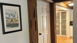 A hallway with a wooden door, a framed painting of a lighthouse, and a kitchen area with cabinets and a microwave.