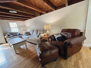 Un salon avec un plafond en bois, un canapé, un fauteuil en cuir, une table basse et une lampe.