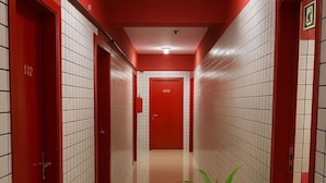 A corridor with red doors, white tiled walls, and a potted plant. - Hotel Londres ADE (Samambaia)