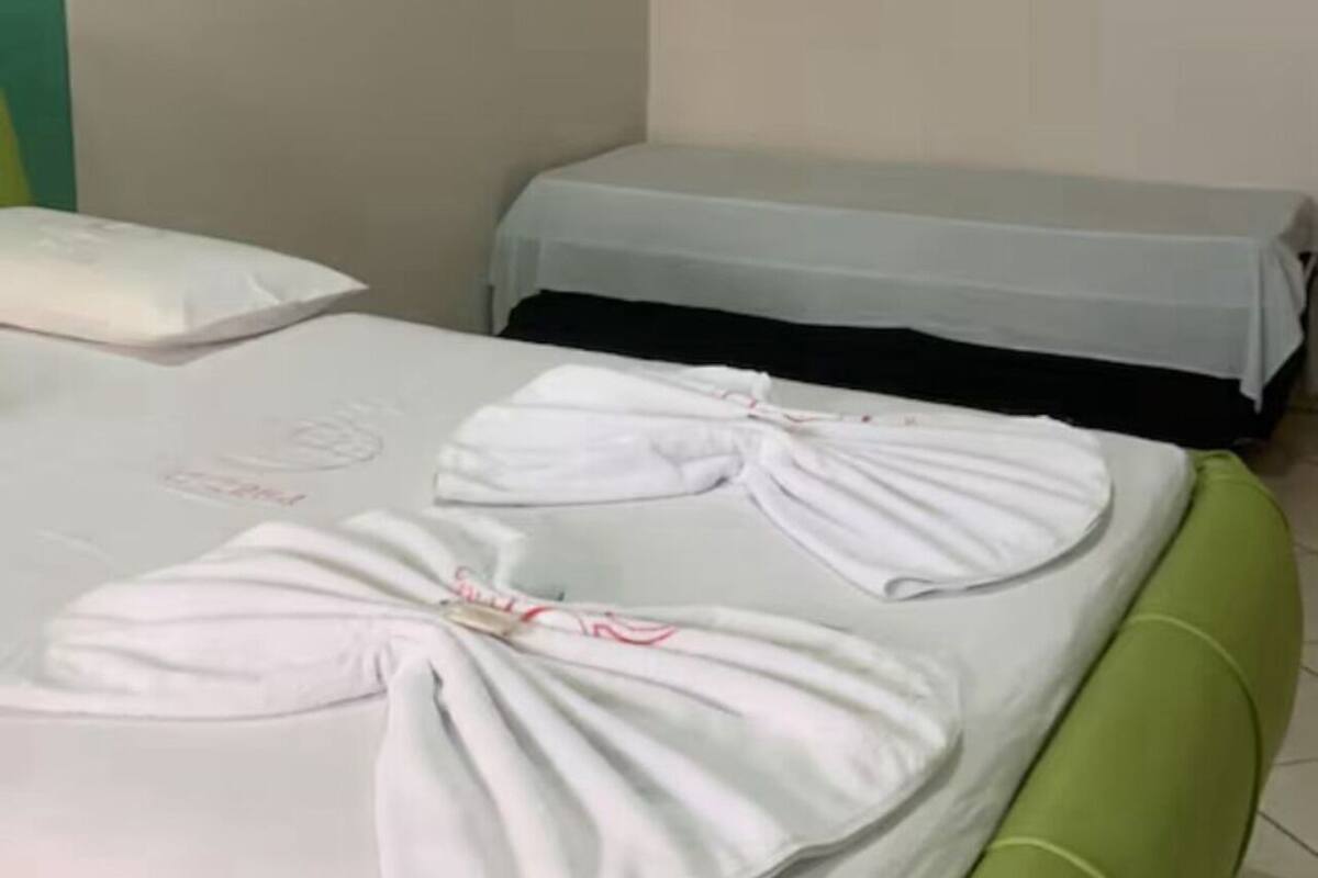 Una habitación de hotel con una cama acolchada de color verde, un cubrecolchón blanco y una almohada blanca.