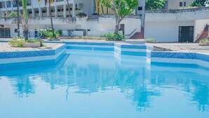 A swimming pool with blue tiles, surrounded by a white building with balconies and a staircase. - GSIH Hotel Diani (Diani Beach)