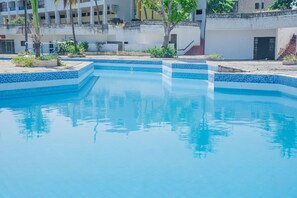 Une piscine aux carreaux bleus, entourée d’un bâtiment blanc doté de balcons et d’un escalier.