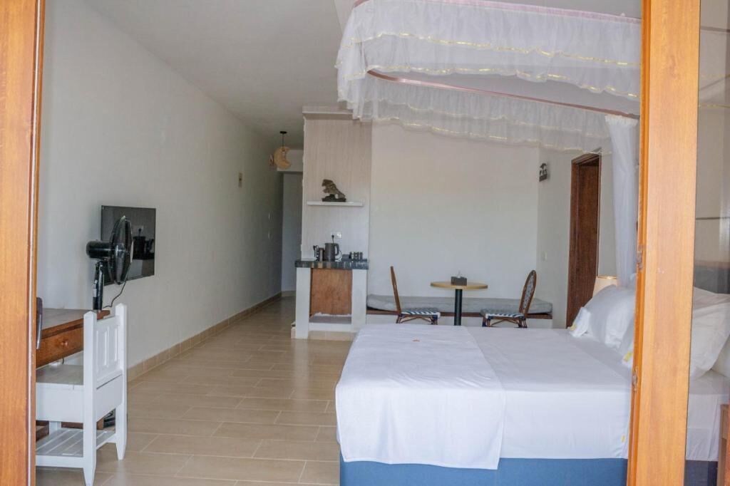 Un dormitorio con cama, escritorio, silla, una mesita y estante con objetos.