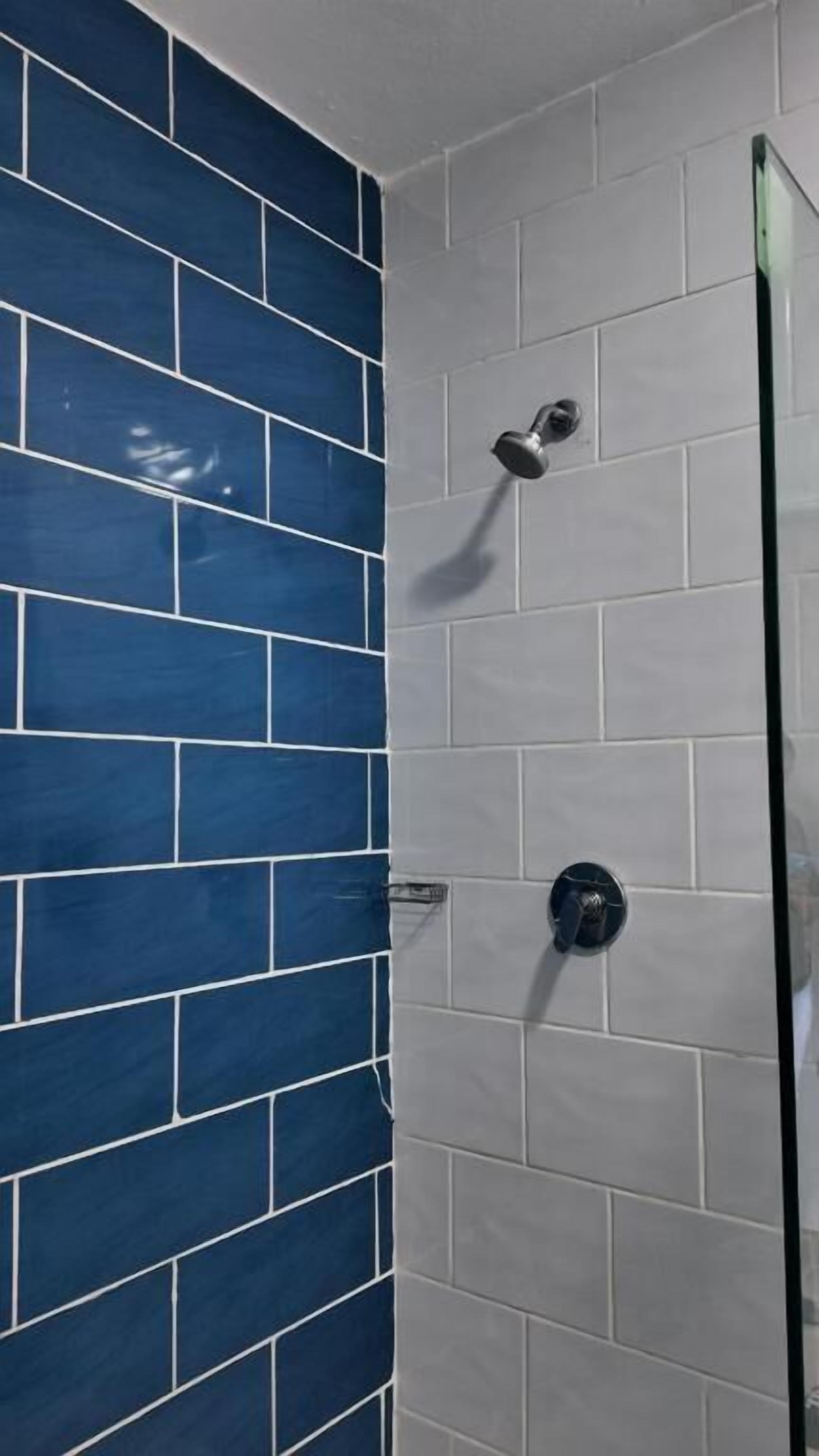 A shower with a glass door, blue and white tiles, and a handheld showerhead.