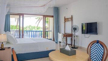 Habitación de hotel con cama, escritorio, silla, televisor y balcón con vista a palmeras.