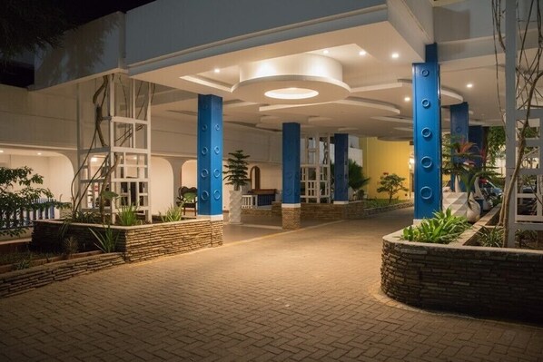 A spacious outdoor area with a paved walkway, blue pillars, and a well-lit entrance. - GSIH Hotel Diani (Diani Beach)