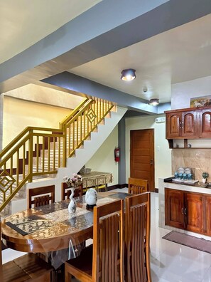 A dining area with a table, chairs, and a vase of flowers. A staircase with a railing leads to another level. - 3BR 2 story Apartment  6 minutes to Airport Fully Fenced/w  cctv and Parking (Puerto Princesa City)