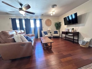 Un soggiorno con un divano in pelle, un tavolino in legno, poltrone a fantasia, una TV e una ventola a soffitto.