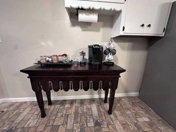 Una mesa de madera oscura con un diseño único, una cafetera y un dispensador de toallas de papel en una habitación con piso de baldosas y un armario blanco.