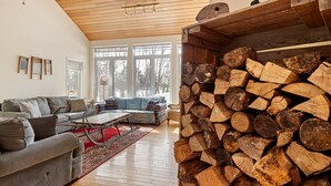 A living room with a sofa, a coffee table, and a fireplace with stacked logs. - Lakeside Memories Await at Trenanthia's Cahoots Cottage (Gravenhurst)