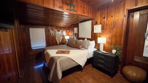 Ein Schlafzimmer mit Holzwänden, einem Bett, Nachttischen und einem kleinen Hocker.