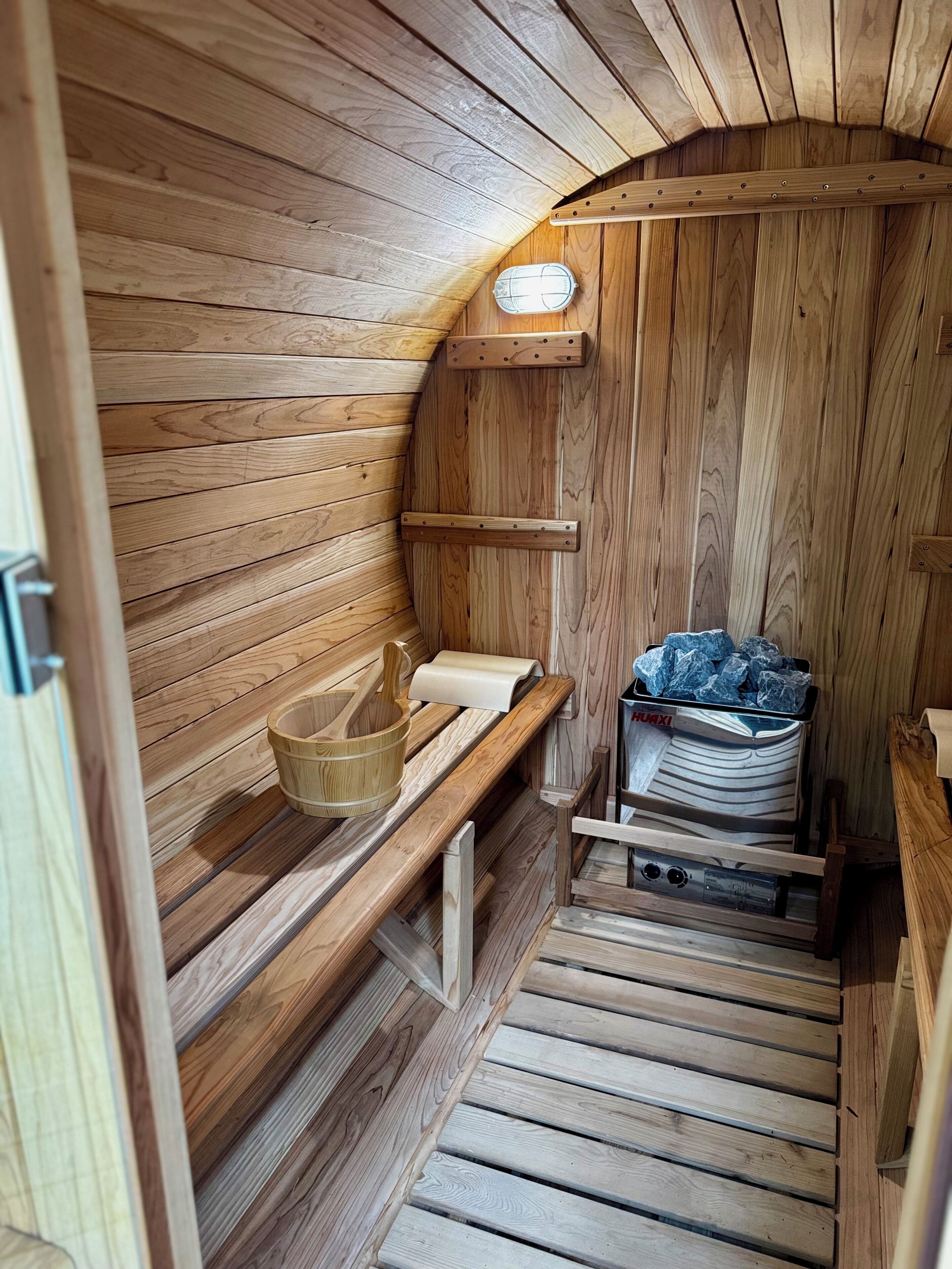Un sauna en bois avec des bancs, un seau en bois, une serviette et un récipient rempli de serviettes.