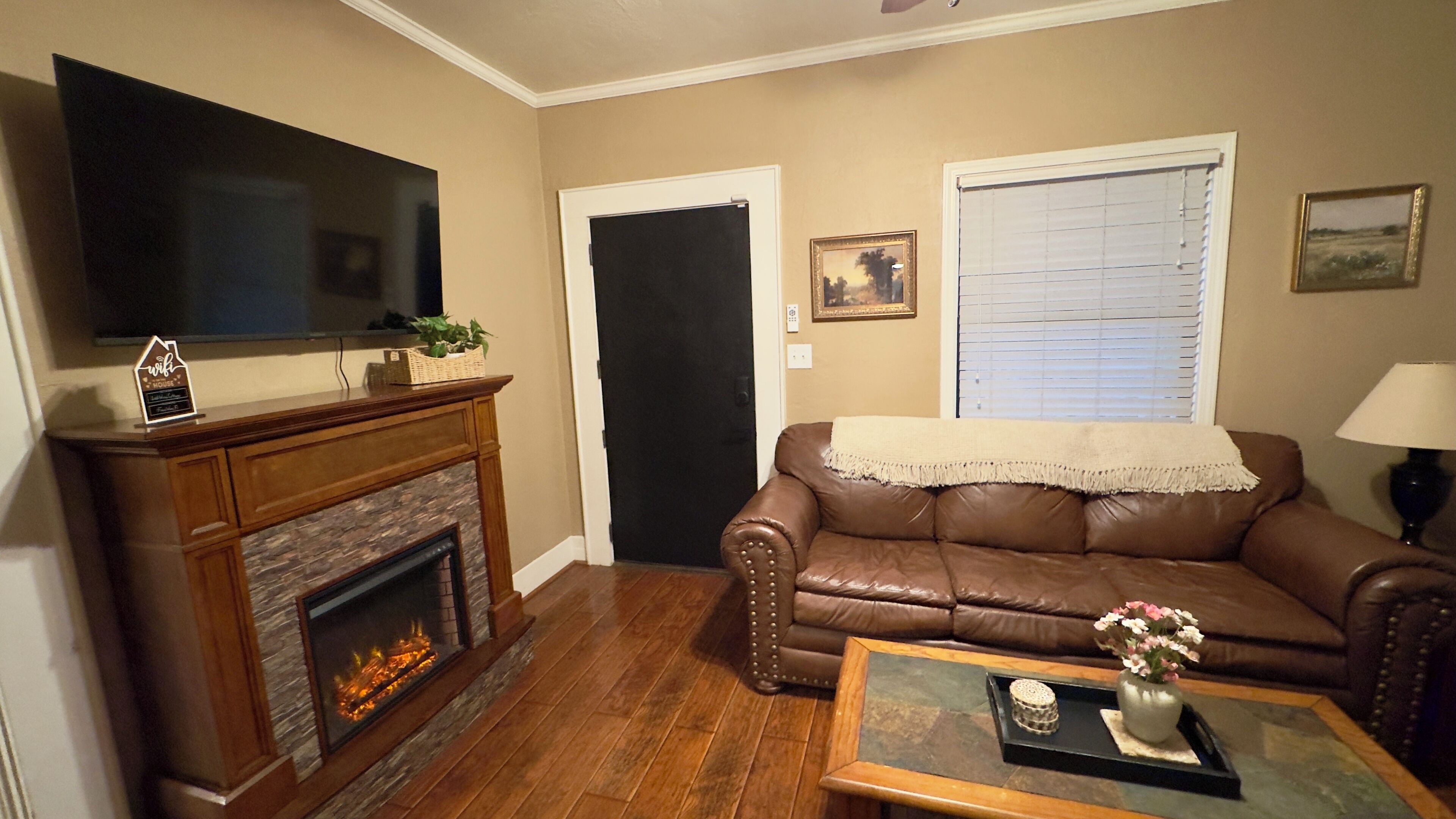 A living room with a fireplace, leather sofa, and a flat-screen TV mounted above it.