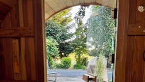 Eine Holzhütte mit Glastür, die zu einem Außenbereich mit einer Bank, einem Blumentopf und einem gepflasterten Weg führt.