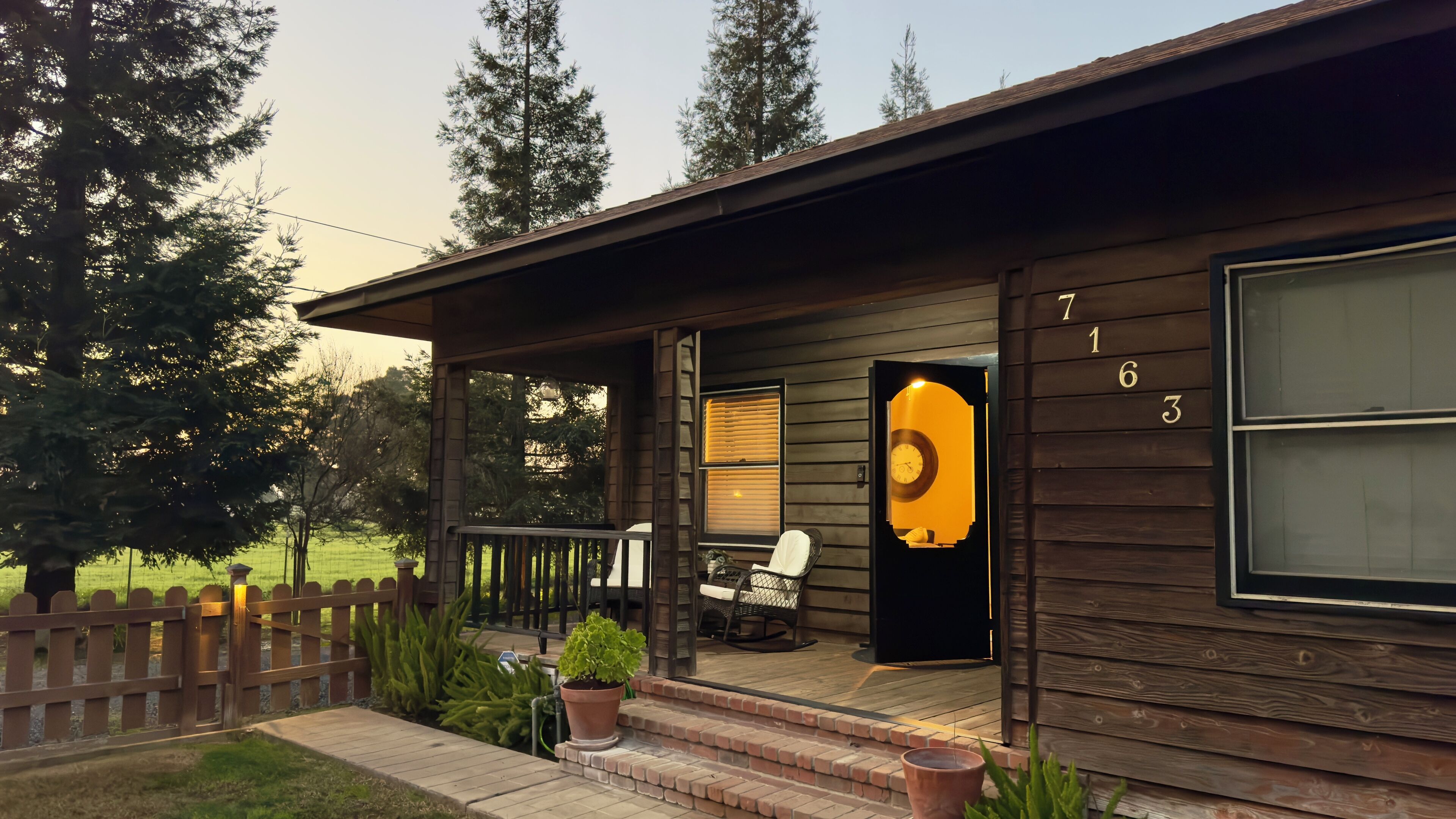 A wooden cabin with a porch, a rocking chair, and a potted plant.
