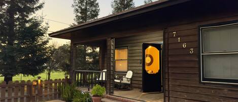 A wooden cabin with a porch, a rocking chair, and a potted plant.