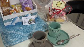 Una mesa con un decantador de vidrio, una caja de pasteles, una taza de café, una cuchara y un mantel individual.