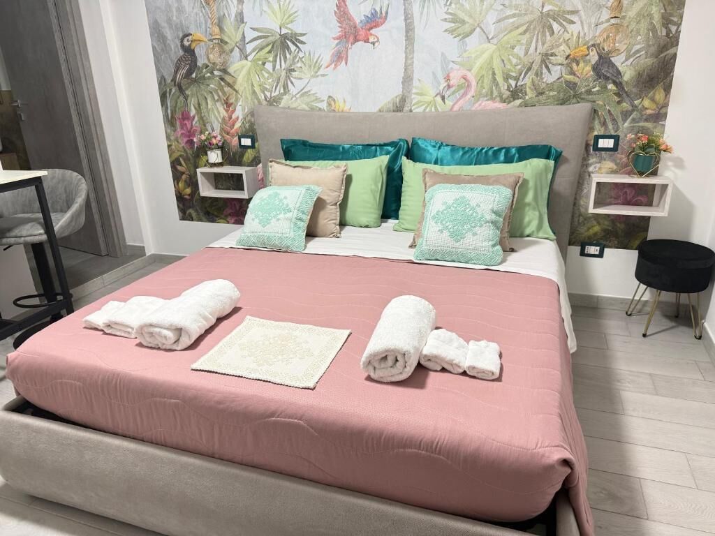 A neatly made bed with pink bedding, a white towel, and a decorative pillow.