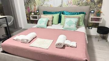 Una cama bien hecha con ropa de cama rosa, una toalla blanca y un cojín decorativo.