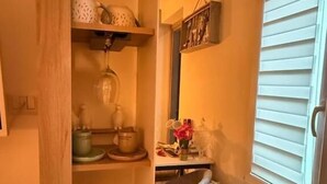 A compact kitchen with a radiator, a window with blinds, and a small table with a vase of flowers. - Umbertos rooms (Jerzu)