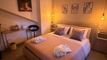 Una cama bien hecha con dos toallas, una mesita de noche con lámpara y una obra de arte en la pared.