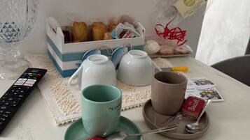 A table with a remote control, a teapot, cups, a teacup, a biscuit packet, and a box of biscuits.
