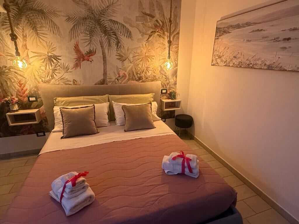 A hotel room with a bed, two nightstands, a wall with a tropical mural, and a painting on the wall.