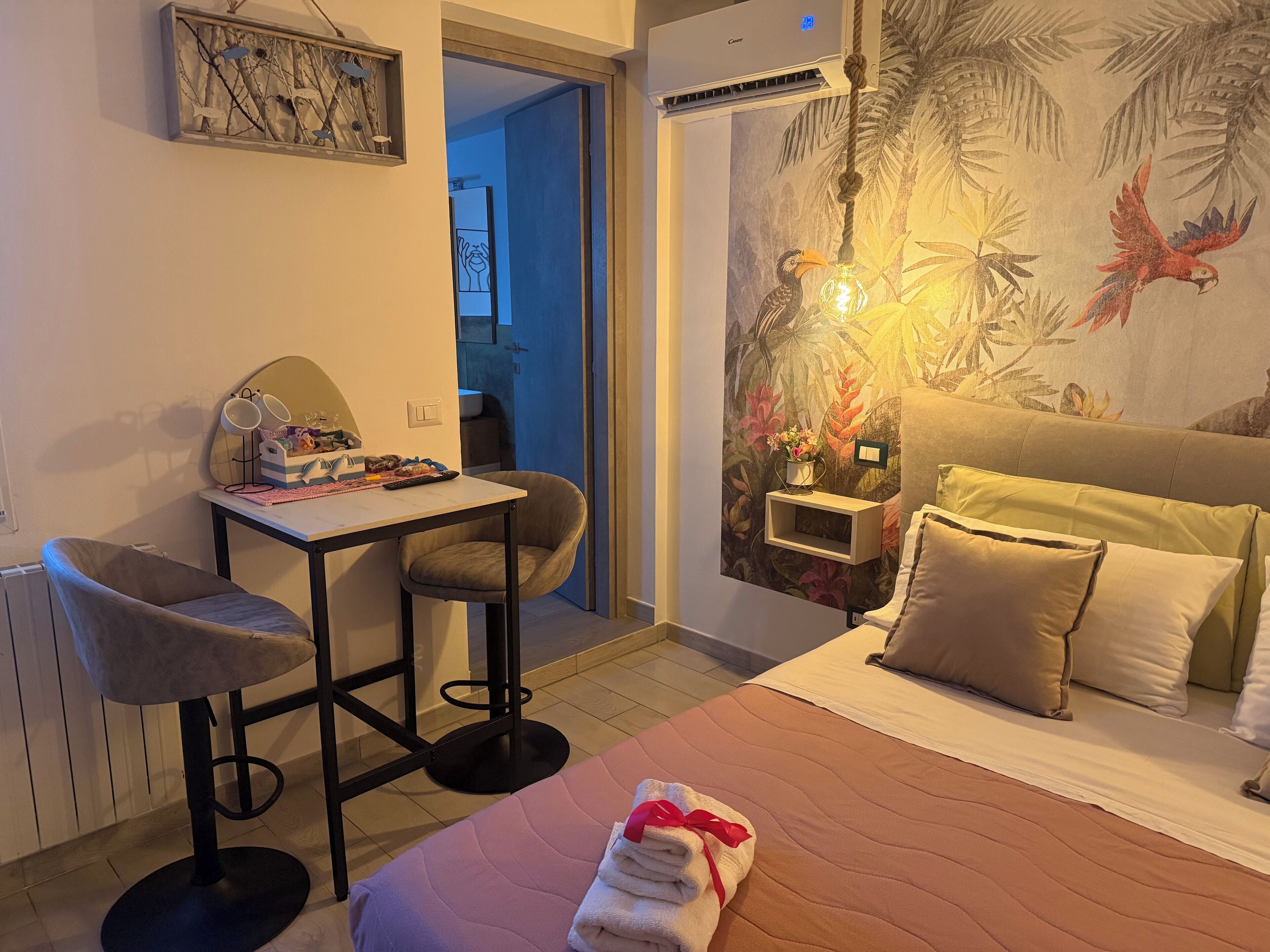 A hotel room with a bed, a desk with a chair, a small table, and a wall with a tropical mural.