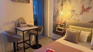 A hotel room with a bed, a desk with a chair, a small table, and a wall with a tropical mural.