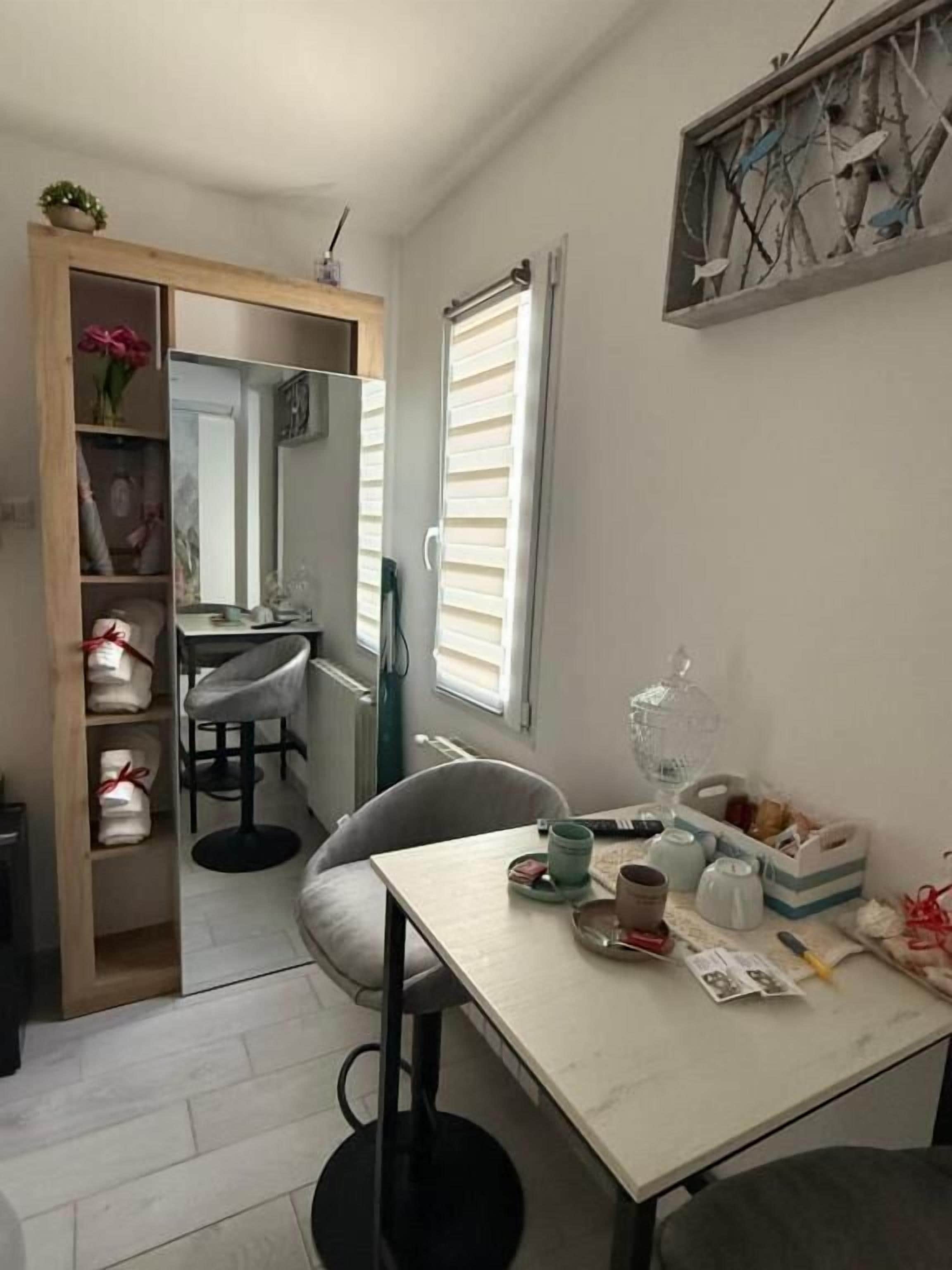 Une pièce de taille modeste, comprenant une petite table, une chaise, une armoire et une fenêtre avec des stores.