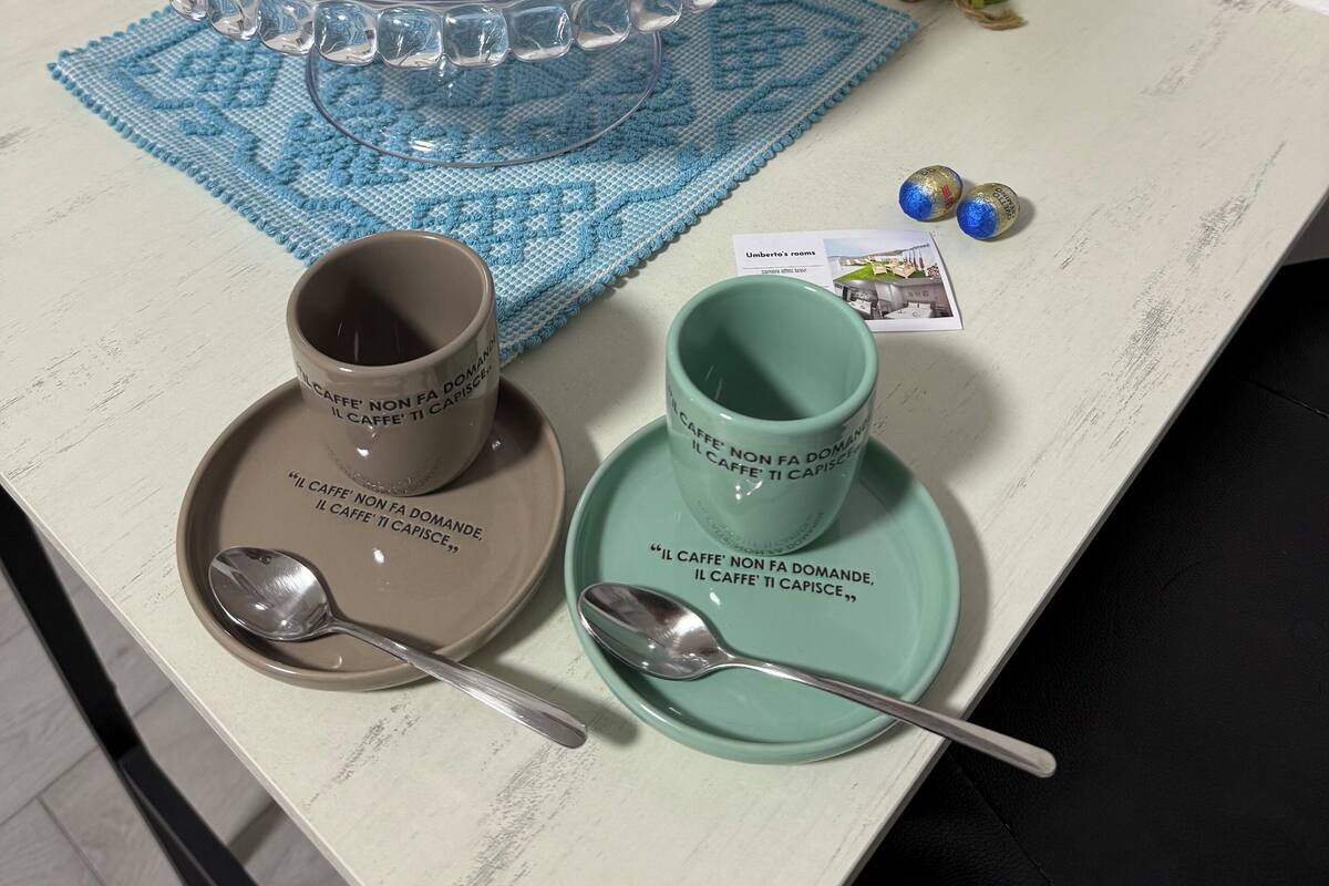 Une table surmontée d’un présentoir en verre transparent contenant des pâtisseries, un set de table bleu en crochet, deux tasses à café assorties de leurs soucoupes et une cuillère.