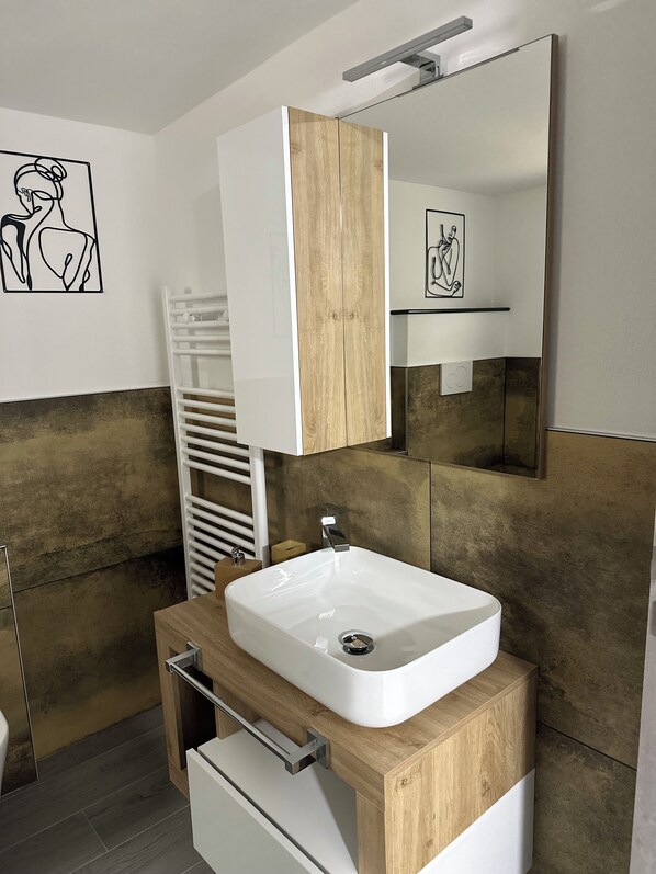 Une salle de bain moderne avec un lavabo blanc, un meuble-lavabo en bois et un grand miroir.