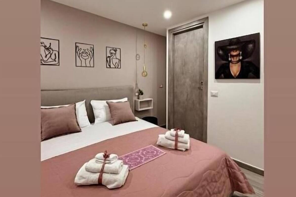 Une chambre à coucher moderne avec un lit, des oreillers, une table de chevet, une commode et des œuvres d’art accrochées aux murs.