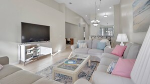 A modern living room with a flat-screen TV, a sofa set, a coffee table, and a dining area in the background. - 15041 Sandpiper Preserve Blvd #202 (Fort Myers)