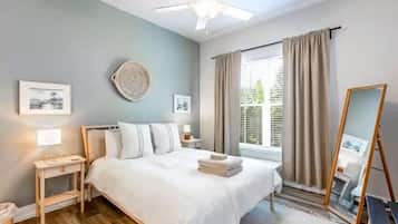 A bedroom with a bed, bedside tables, a ceiling fan, a window with curtains, and artwork on the walls.