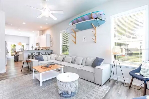 A modern living room with a sectional sofa, a coffee table, a round ottoman, and a ceiling fan. - Blue Bungalow · Walk Downtown · Near UF & Shands · Fenced Yard · PS5 (Gainesville)
