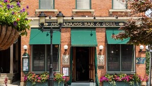 Tiilestä rakennettu rakennus, jossa on vihreä markiisi ja kyltti, jossa lukee: ”Old Adams Bar & Grill”.