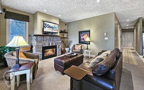 A living room with a stone fireplace, a television mounted above it, and a sofa with a side table. - Bighorn Resort 3BR Condo Getaway (Radium Hot Springs)