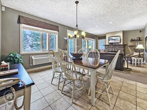 A dining area with a table and chairs, a chandelier, and a view of the outdoors through large windows. - Bighorn Resort 3BR Condo Getaway (Radium Hot Springs)