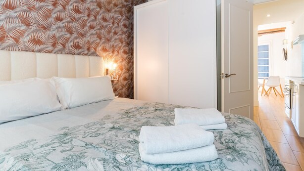 Un dormitorio con una cama, una mesita de noche, una lámpara de pared y una puerta que da al baño.