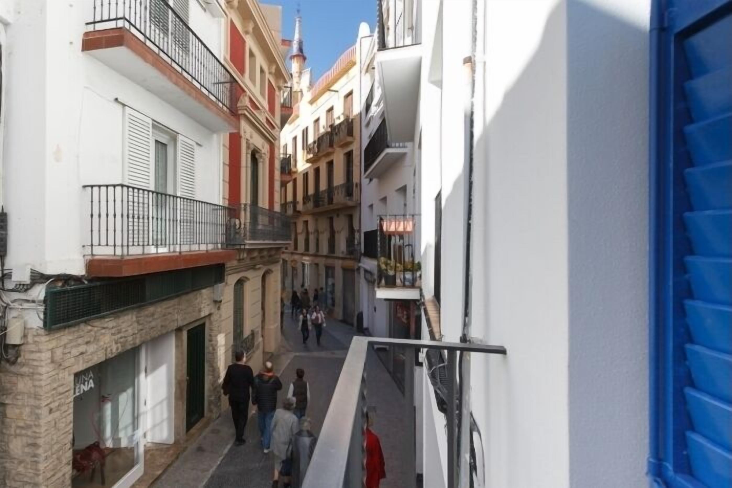 A narrow street with buildings on either side, a blue door on the right, and people walking.
