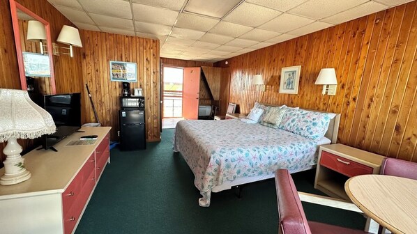 A room with a bed, a desk, a chair, a table, a refrigerator, and a television. - Sea Foam Motel (Nags Head)