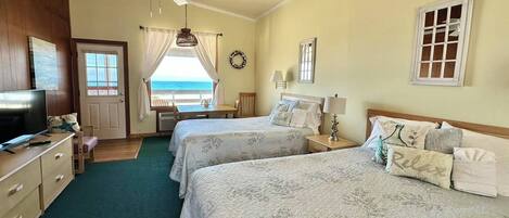 A hotel room with two beds, a TV, a desk, and a view of the ocean.
