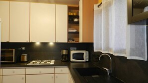 Una cucina compatta con mobili bianchi, un piano di lavoro nero, un forno a microonde, una macchina per il caffè e un lavello con rubinetto.