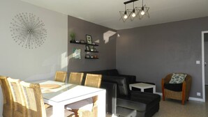 Un soggiorno moderno con zona pranzo, caratterizzato da un tavolo con piano in vetro, sedie in vimini, un divano nero e un piccolo tavolino.