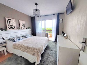 A bedroom with a bed, bedside table, lamp, artwork, and a TV on the wall. - 3-room apartment, 6 beds, parking in Bormes-les-Mimosas (Bormes-les-Mimosas)